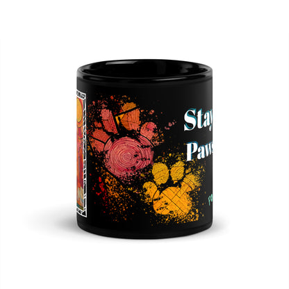 Stay Pawsitive text with image of a Pomeranian dog on stained glass style background with colorful paw prints on a black ceramic mug 11 oz — front view