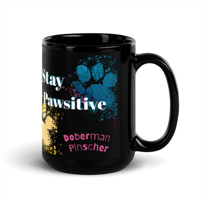 Stay Pawsitive text with image of a Doberman Pinscher dog on stained glass style background with colorful  paw prints on a black ceramic mug 15 oz — handle on right
